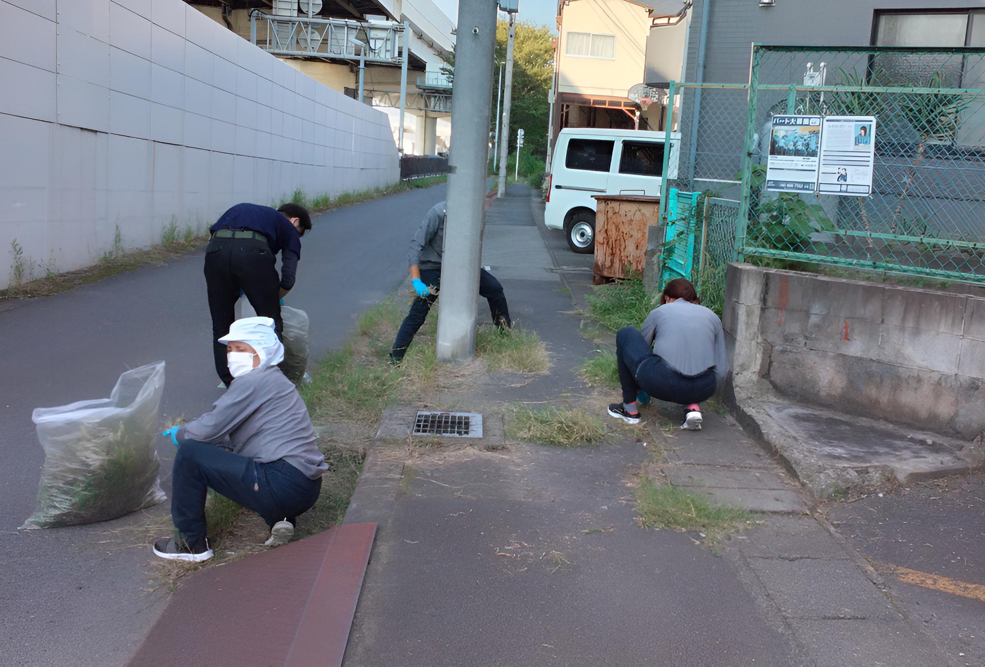 三和紙工会社駐輪場前の歩道に生えた雑草をむしる従業員たち